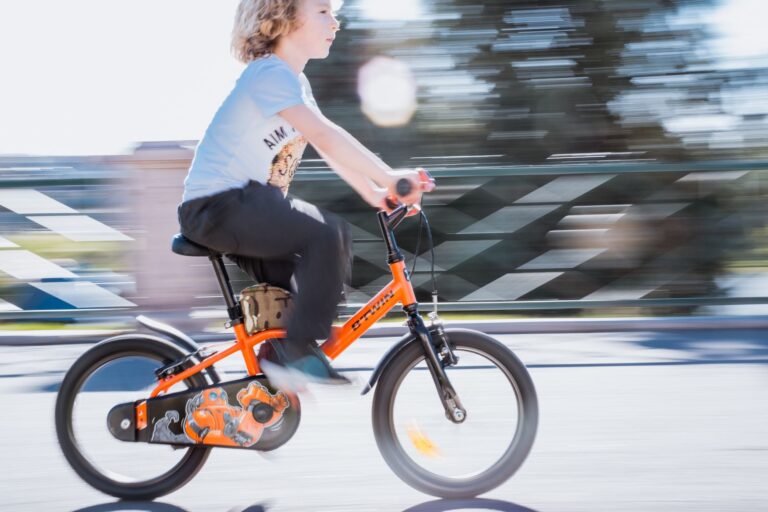 Young boy riding orange bicycle outdoors in Türkiye, showcasing motion and excitement.