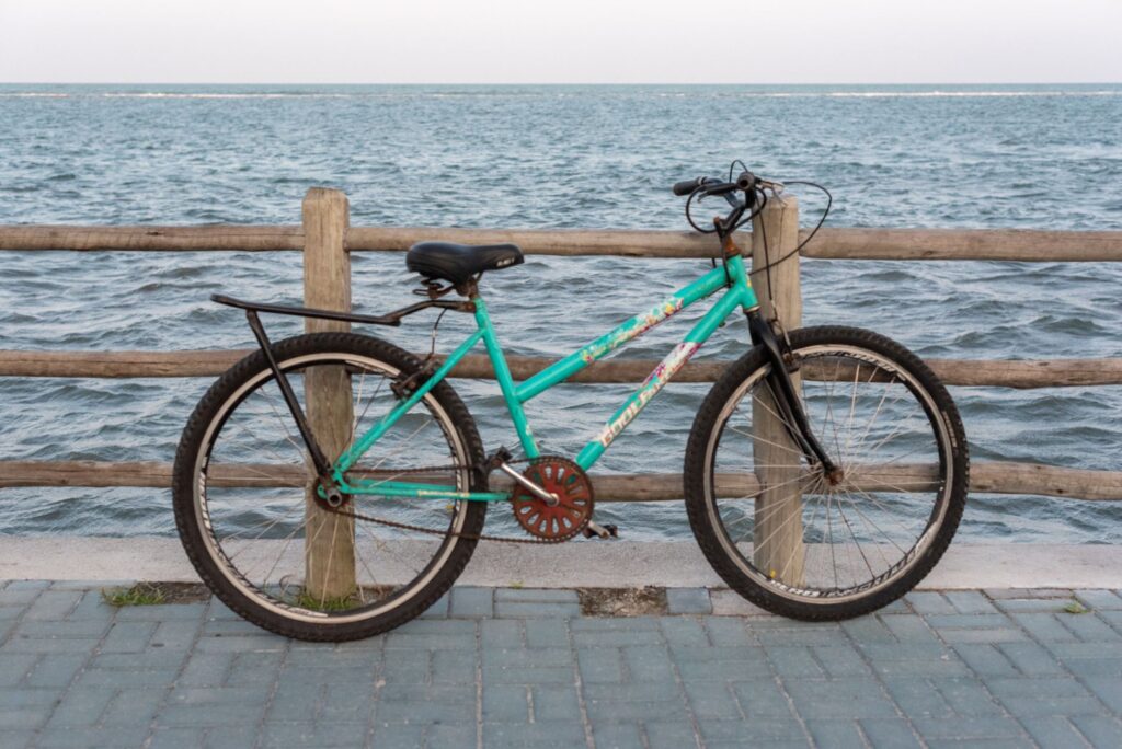 A vibrant green bicycle rests against a wooden fence overlooking the ocean in Porto Seguro, Brazil.