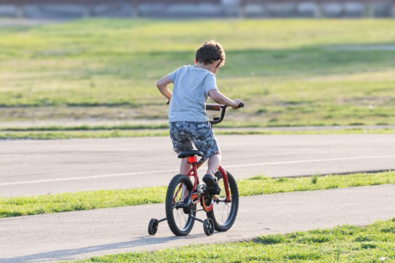 Young boy riding a bicycle with training wheels in a park on a sunny day.