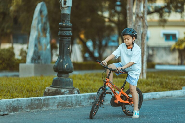 Young boy with helmet rides orange bicycle in a park.