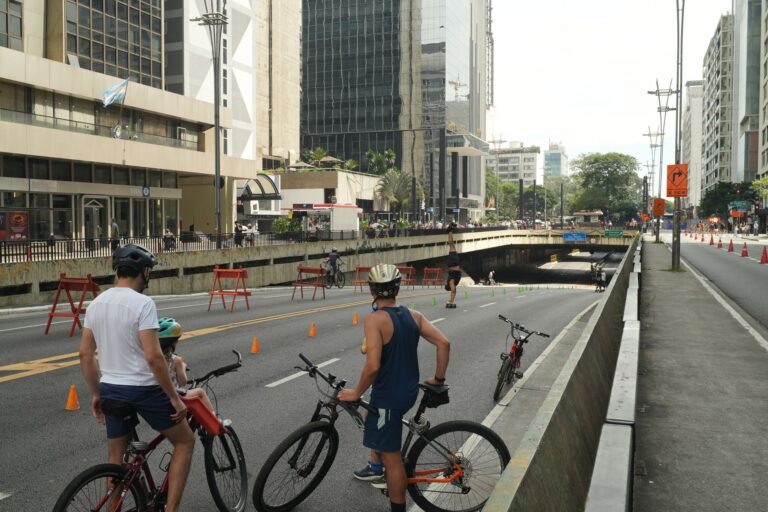 People cycling on Avenida Paulista in São Paulo during a car-free event, showcasing urban life.