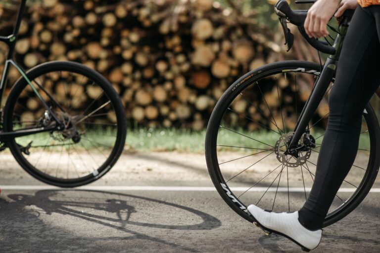 Close-up of cyclists on a sunlit road by a woodland, with focus on wheels and bike frame.