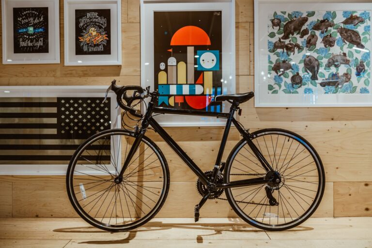 Black bicycle parked indoors against a wall with framed art, creating a stylish and modern look.