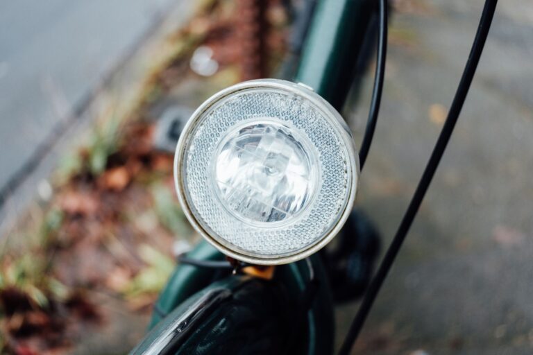 Detailed close-up of a bicycle headlight against an urban outdoor backdrop, showing clear lens design.