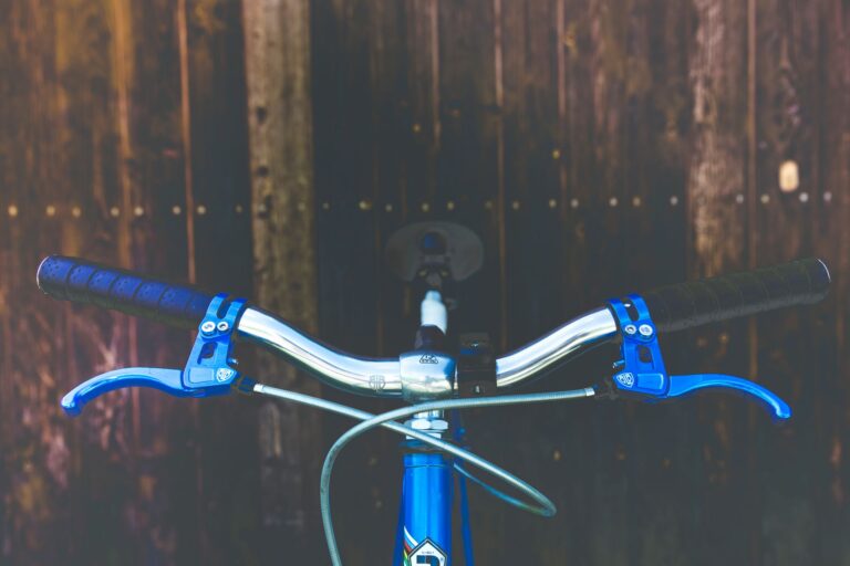 Detailed view of a bicycle handlebar with blue brake levers on a wooden backdrop.
