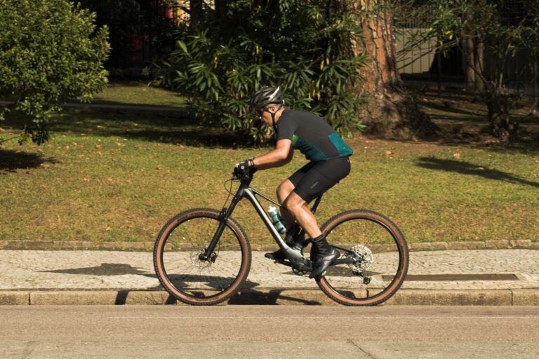 Man riding a mountain bike on a sunny city street, wearing safety gear and sportswear.