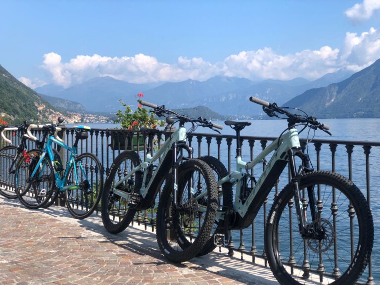 Bicycles lined up by a scenic view of Lake Como and surrounding mountains under a clear blue sky.