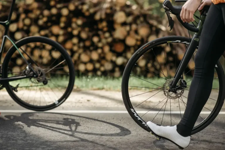 Close-up of cyclists on a sunlit road by a woodland, with focus on wheels and bike frame.