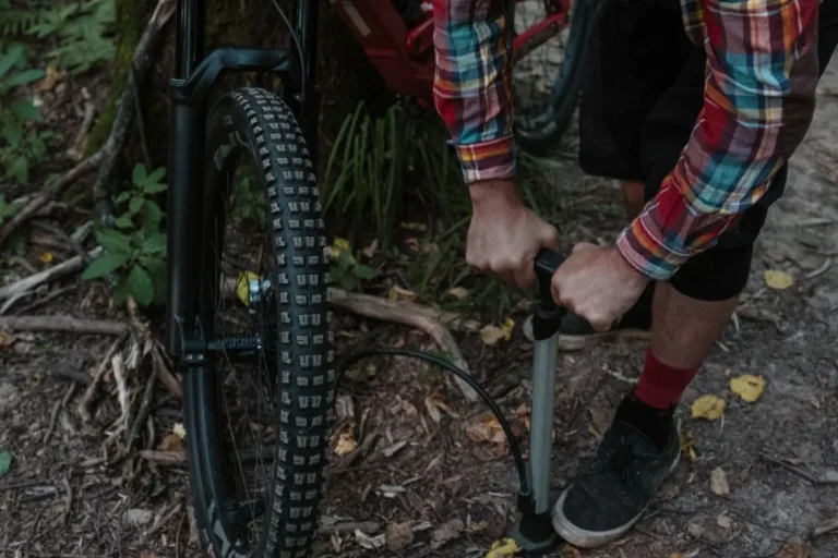 A cyclist uses a pump to inflate a bicycle tire while in a forested area.