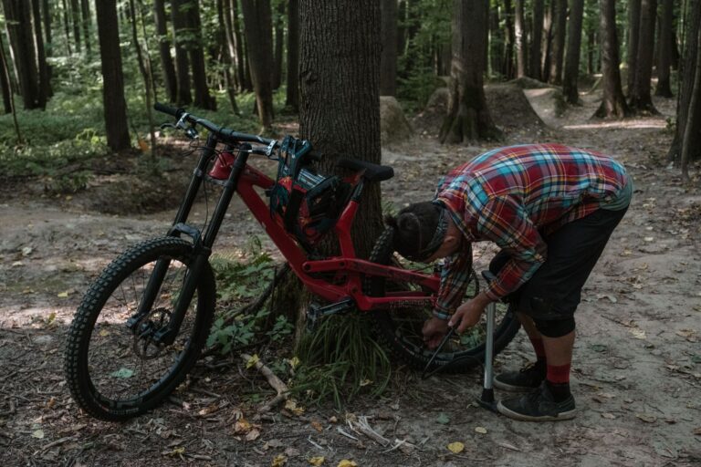 A man fixes a bicycle in a forest during summer, capturing outdoor adventure.