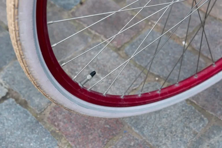 Detailed close-up of a red bicycle wheel with spokes and valve on cobblestone.