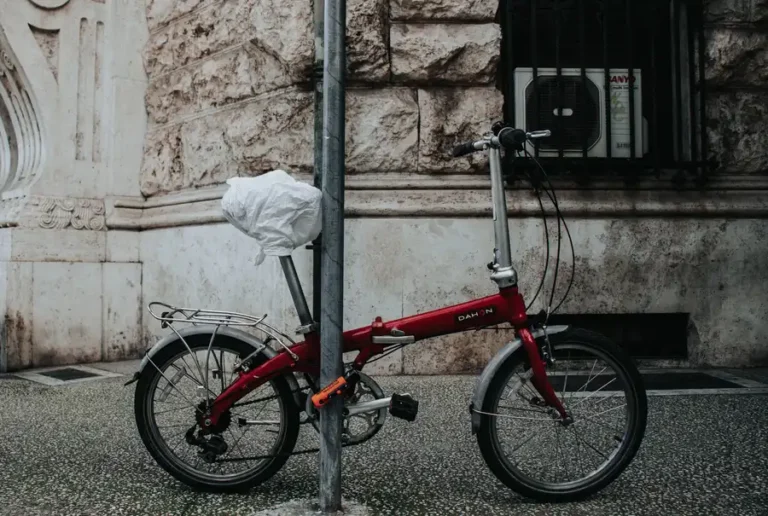 A chained red folding bicycle against a textured stone wall captured on an urban street.