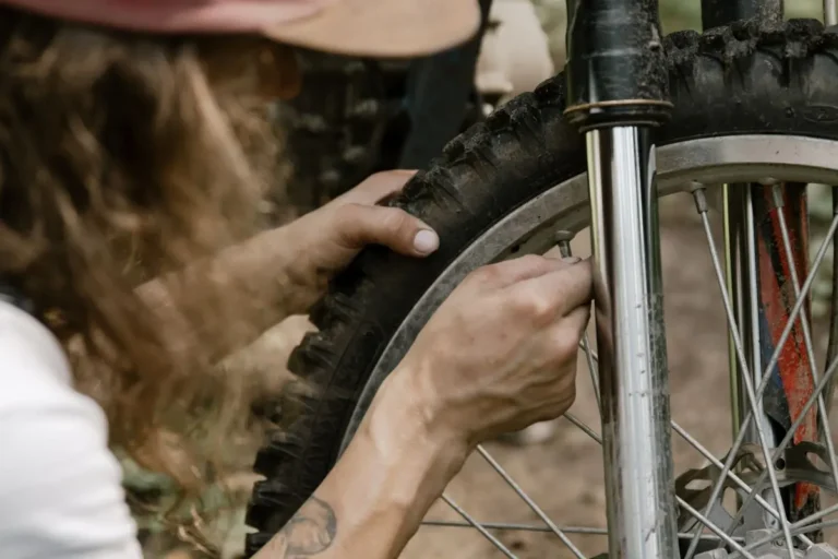Close-up of mechanic's hands fixing a dirt bike tire in an outdoor setting.