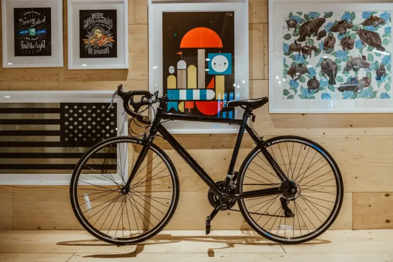 Black bicycle parked indoors against a wall with framed art, creating a stylish and modern look.