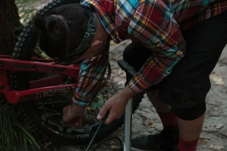 A cyclist inflates a mountain bike tire in a forest setting, ready for a downhill adventure.